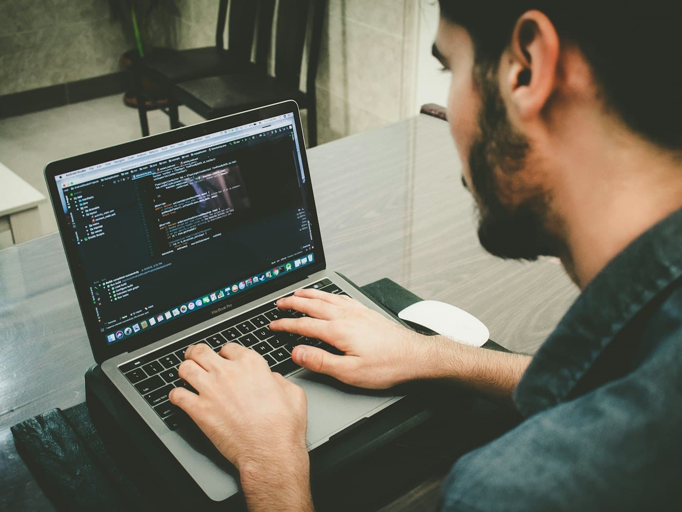 Over-the-shoulder view of a programmer's hands typing on a laptop showing code in an editor.