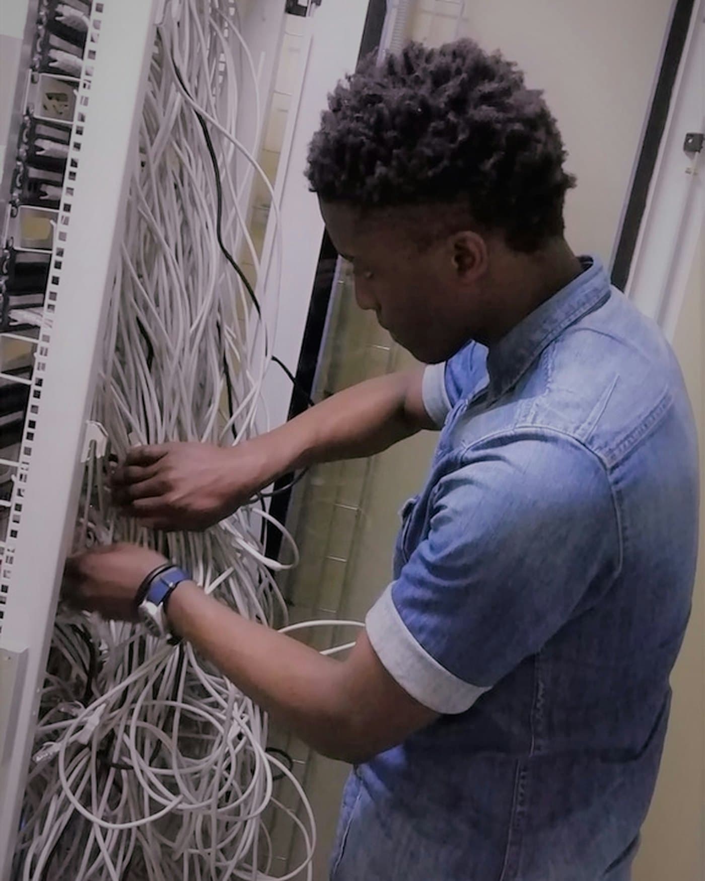A technician in a denim shirt dresses bundles of network cable inside an equipment rack.
